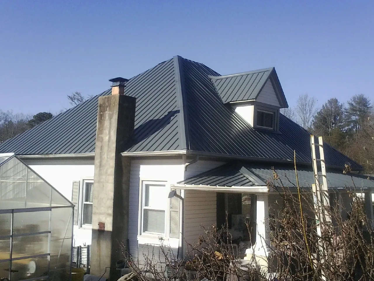 Dark blue standing seam metal roof on a white farmhouse with dormer — Slate & Tile Roof Repair by Roofing Brothers in Ruby